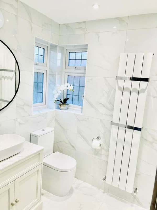 Melanie Levy's bright bathroom showing the white marble walls and white sink unit and toilet